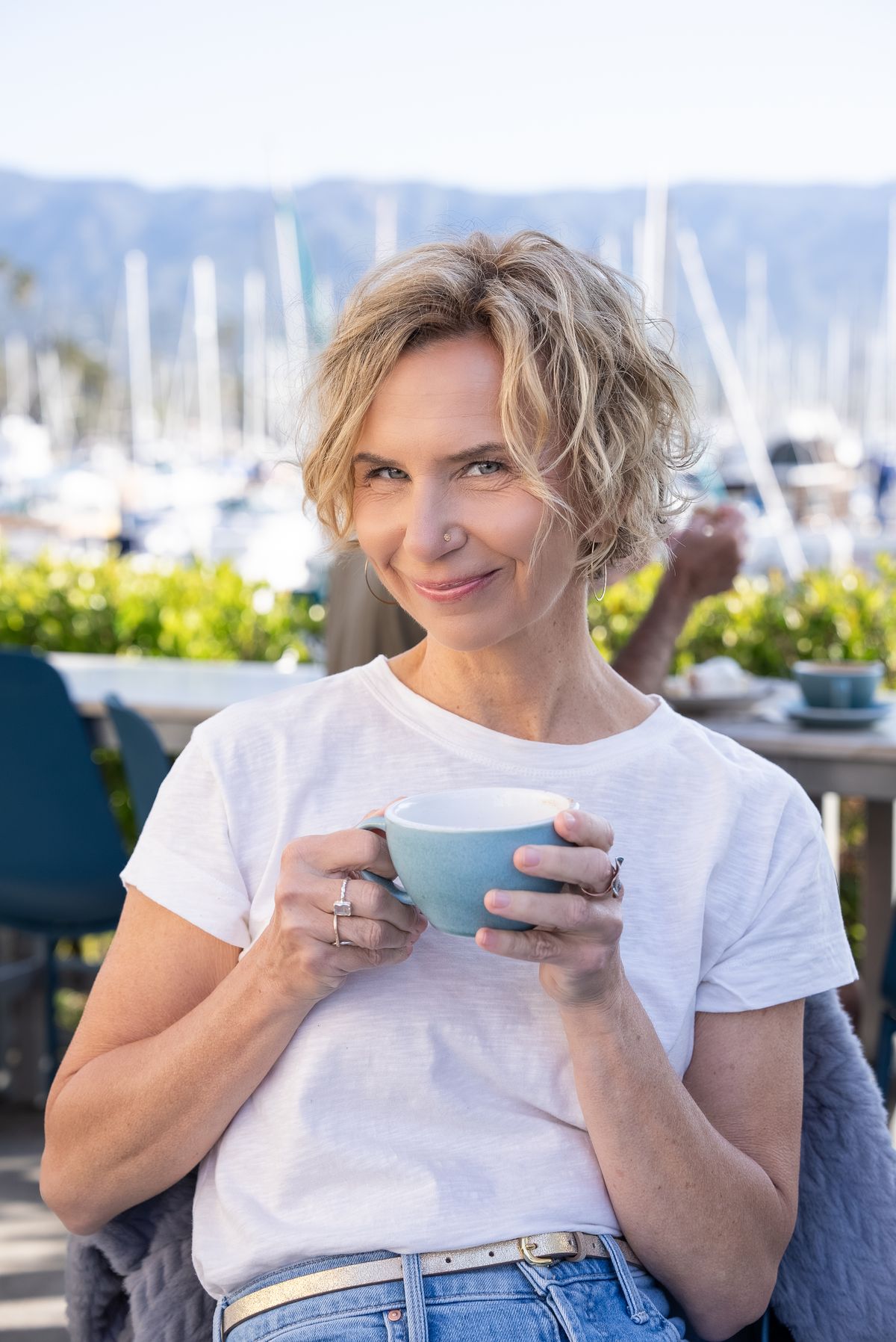 Michelle smiling over a cup of coffee at a harborside table